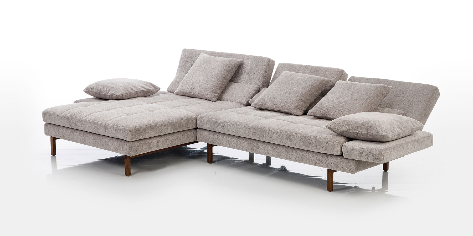Eckgarnituren von brühl Eine Eckgarnitur in sandfarbenem Stoff mit einem Longchair mit abgeklappter Armlehne links sowie einem Anstellsofa mit leicht abgesenkten Rückenlehnen. Auf der Garnitur liegen vier Kissen.