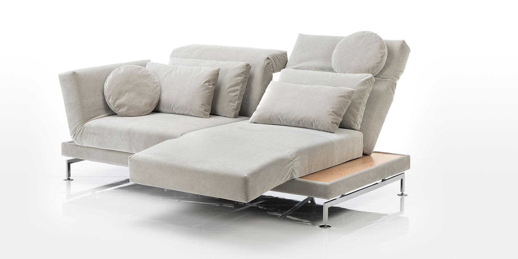 Sofa brühl moule large Ein Sofa mit zwei Sitzplätzen in einem dunklen beige. Der rechte Sitz wurde um 90 Grad gedreht und die Armlehne so abgesenkt, dass sie als Fußstütze verwendet werden kann. Auf dem Sofa wurden vier rechteckige sowie zwei runde Kissen drapiert.