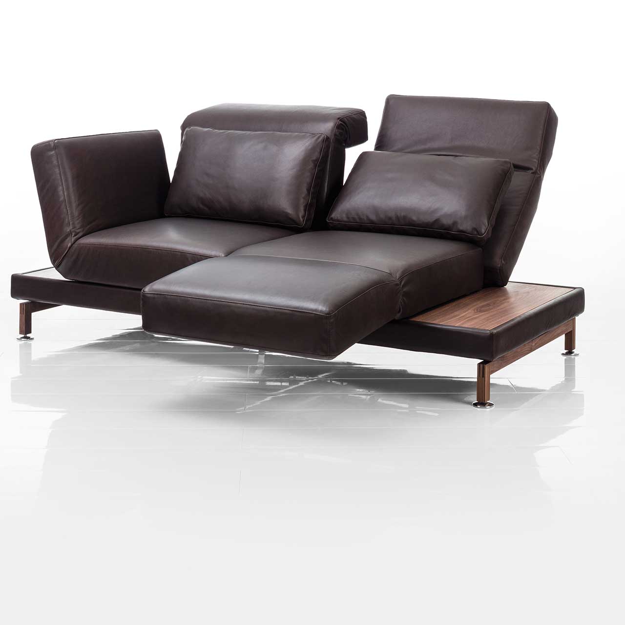 brühl moule small - Sofa 73207 Dunkelbraunes Ledersofa. Rechts und links neben den Armlehnen befinden sich schmale Ablageflächen in dunklem Holz. Die rechte Armlehne ist als Fußsütze vorgeschwenkt, die Rückenlehne leicht abgesenkt.