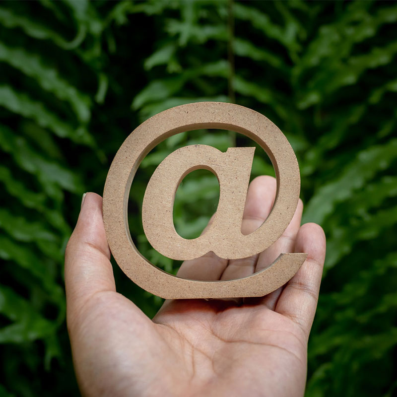 Link: Newsletter-Anmeldung. Eine Hand hält ein hölzernes @ Zeichen.