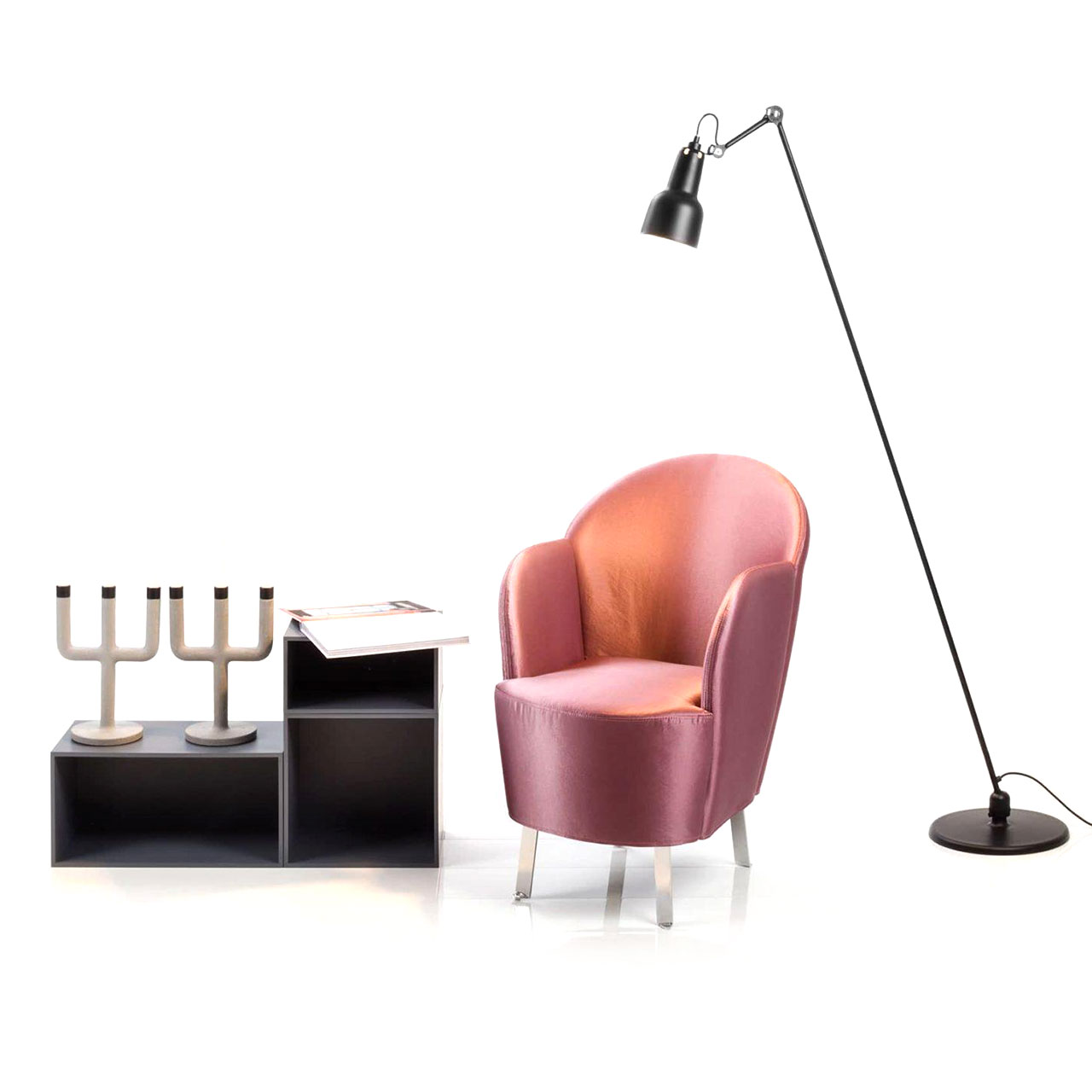 brühl floret Sessel 65801 Ein Sessel mit Füßen aus verchromten Flachstahl und mit einem glänzenden Stoff in der Farbe Rose bezogen steht zwischen einem niedrigen Regal und einer Stehlampe.