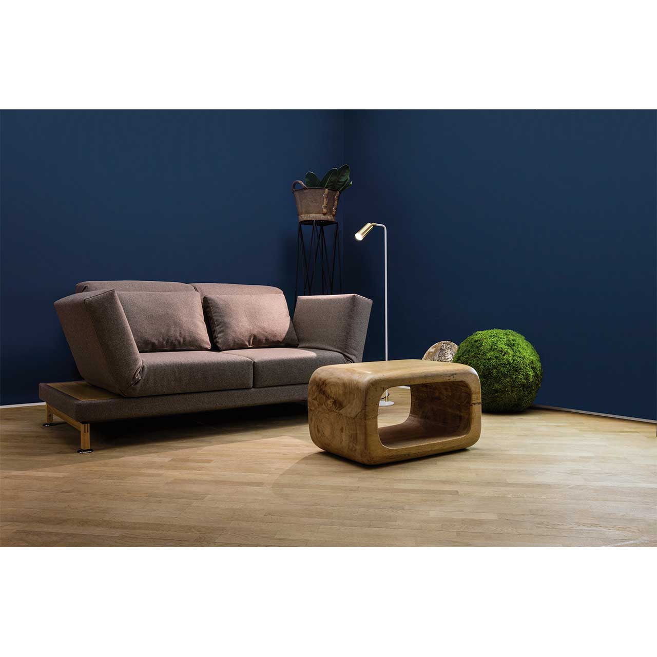brühl moule small - Sofa 73207 Ambientebild. Braunes Stoffsofa mit Kufen in Holz. Rechts und links neben den Armlehnen befinden sich schmale Ablageflächen in hellem Holz. Rechts neben dem Sofa steht eine Stehlampe, vor dem Sofa steht ein Couchtisch aus Holz.