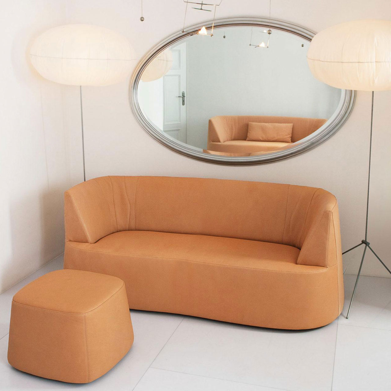 brühl powder Hocker 58861 Ambientebild: Ockerfarbenes Sofa mit passendem Hocker vor einer weißen Wand. An der Wand hängt ein ovaler Spiegel mit silbernen Rahmen.