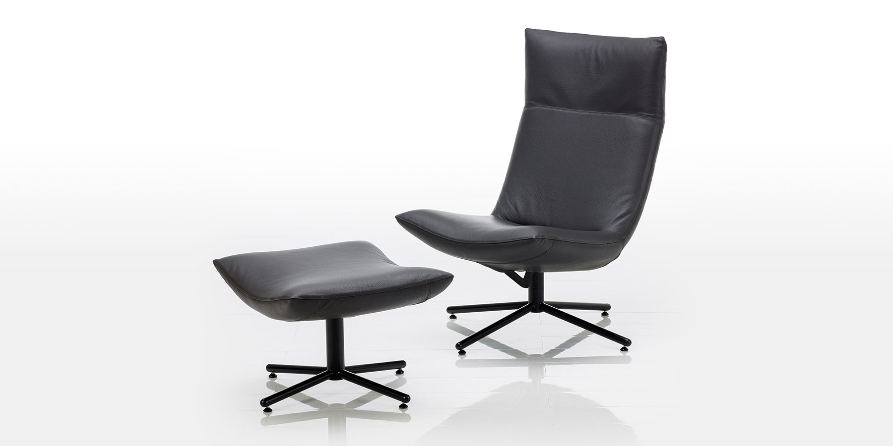 Hochlehnsessel brühl gerard Ein Drehsessel aus schwarzem Leder ohne Armlehnen mit einem schwarzen Kreuzfuß. Daneben steht der passende Hocker, ebenfalls in schwarzem Leder und auf einem schwarzen Kreuzfuß. Die Sitzflächen sind nach unten gewölbt.