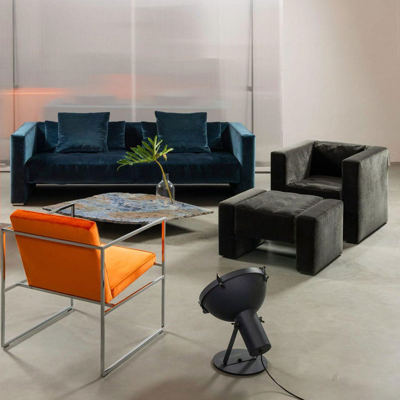 brühl visavis Sofa 21713 Ambientebild. Im Hintergrund stehen ein Sofa und ein Wohnzimmertisch. Der Fokus liegt auf einem schwarzen Sessel mit dazu passendem Hocker.