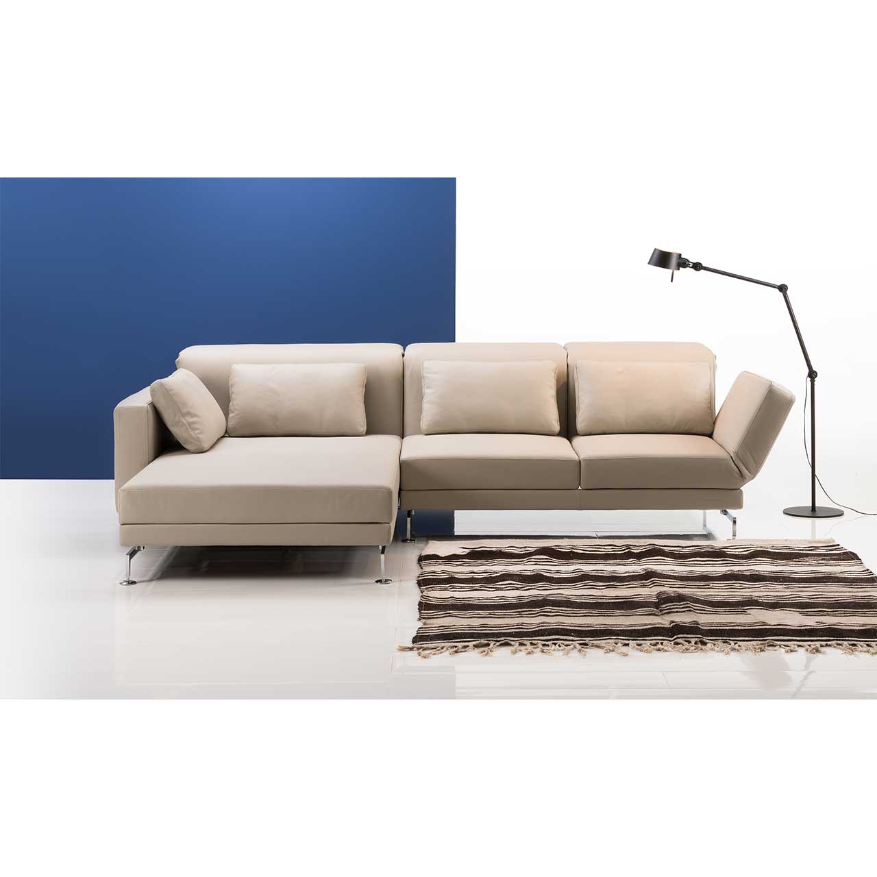 brühl moule-medium - Sitzgruppe 73138 + 73123 Eckgarnitur mit breitem Longchair links in beigem Leder. Rechts daneben steht eine Lampe, vor der Garnitur liegt ein gestreifter Teppich.